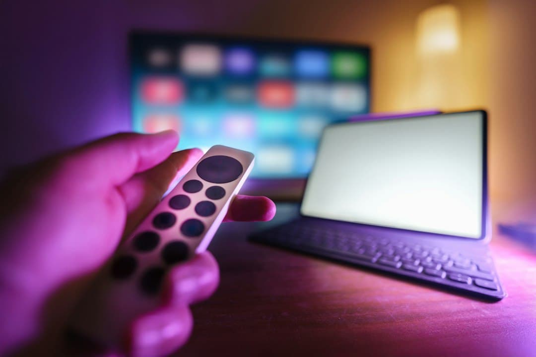Hånd med fjernbetjening foran tv og tablet – IPTV smart player-app